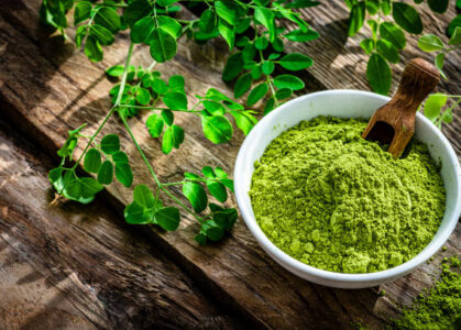 Moringa Nutritional supplement: high angle view of Moringa oleifera powder in a white bowl shot on rustic wooden table. Green Moringa leaves are around the bowl. High resolution 42Mp studio digital capture taken with Sony A7rII and Sony FE 90mm f2.8 macro G OSS lens